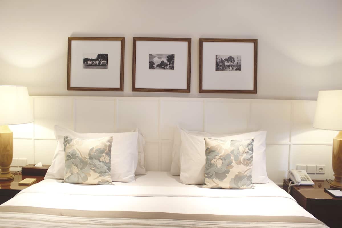 Une chambre d’hôtel avec un lit soigneusement fait, deux lampes de chevet, une table de chevet avec un téléphone et trois tableaux encadrés accrochés au mur.