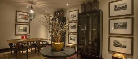 A dining area with a round table, chairs, a vase with branches, and framed pictures on the walls.