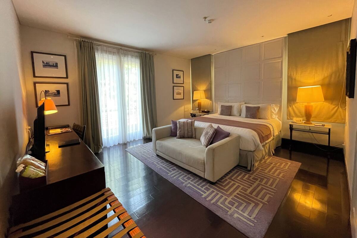 Une chambre d’hôtel avec un lit, un canapé, un bureau, une lampe et une fenêtre avec des rideaux.