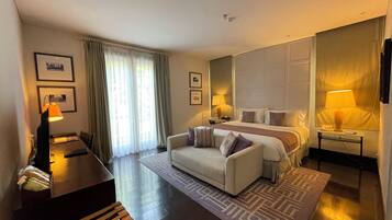 Habitación de hotel con cama, sofá, escritorio, lámpara y ventana con cortinas.