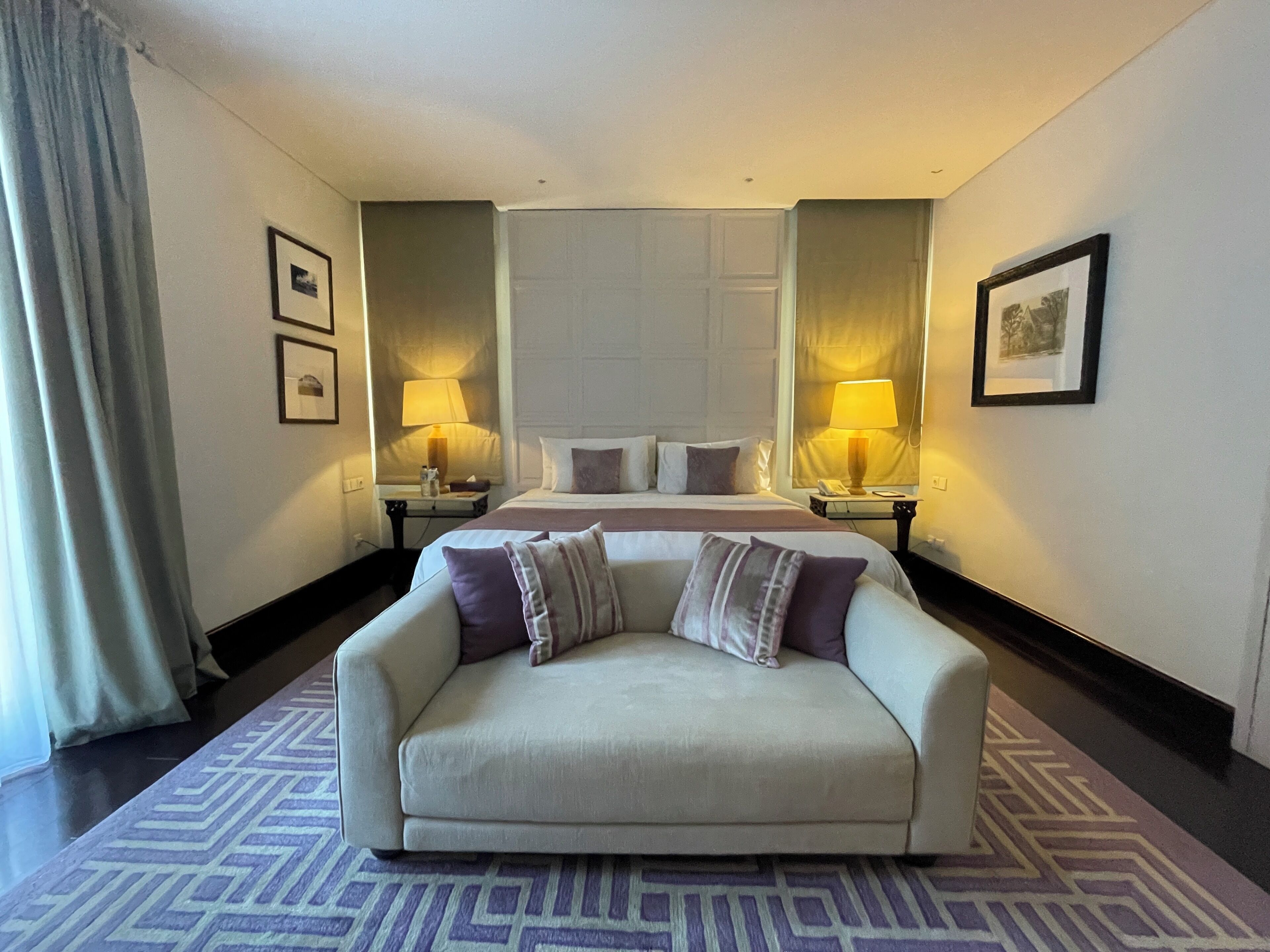 Une chambre d’hôtel avec un lit, deux tables de chevet avec des lampes, un canapé et un tapis à motifs.
