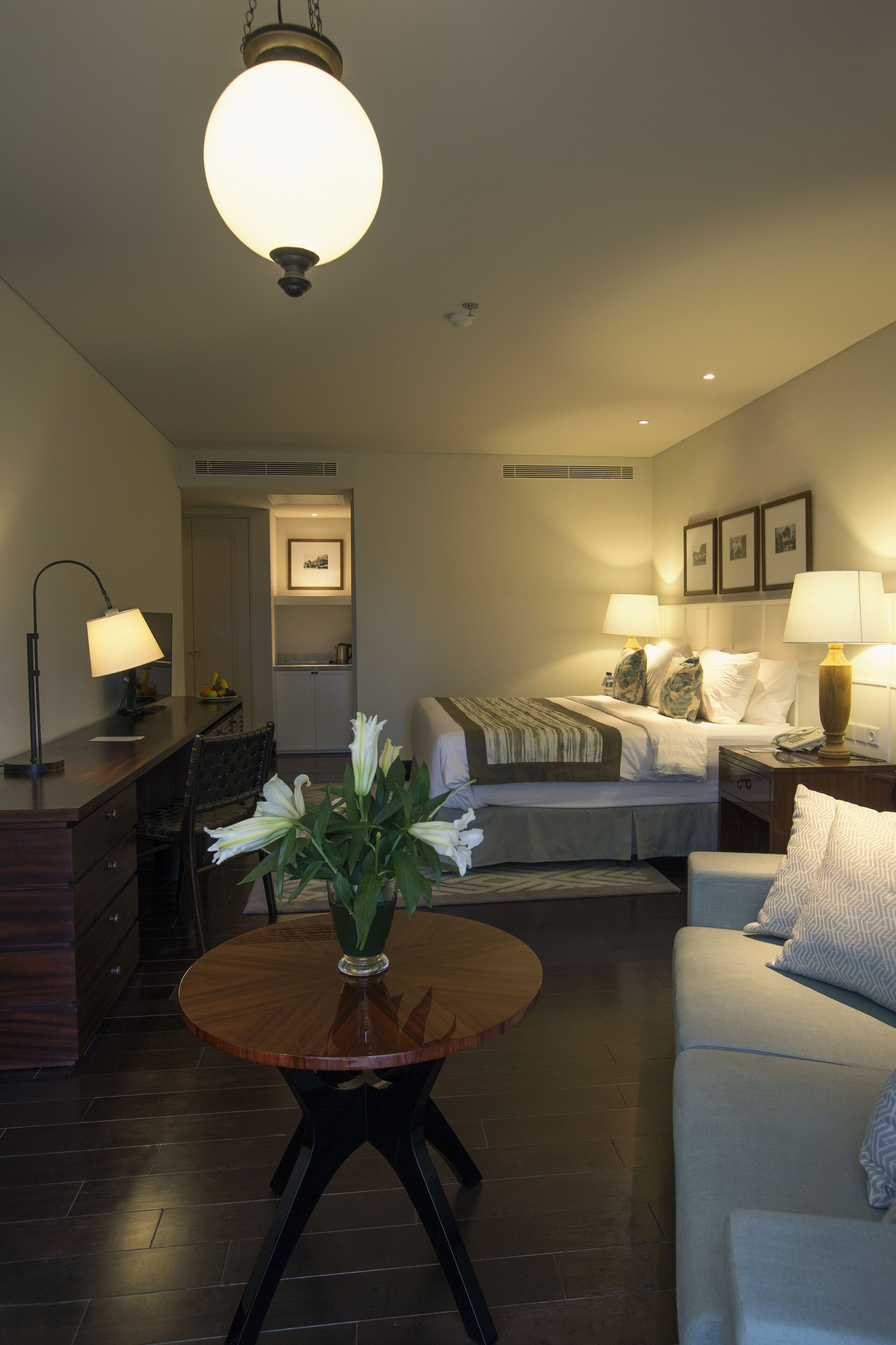 A hotel room with a bed, a sofa, a desk, a lamp, and a vase with flowers.