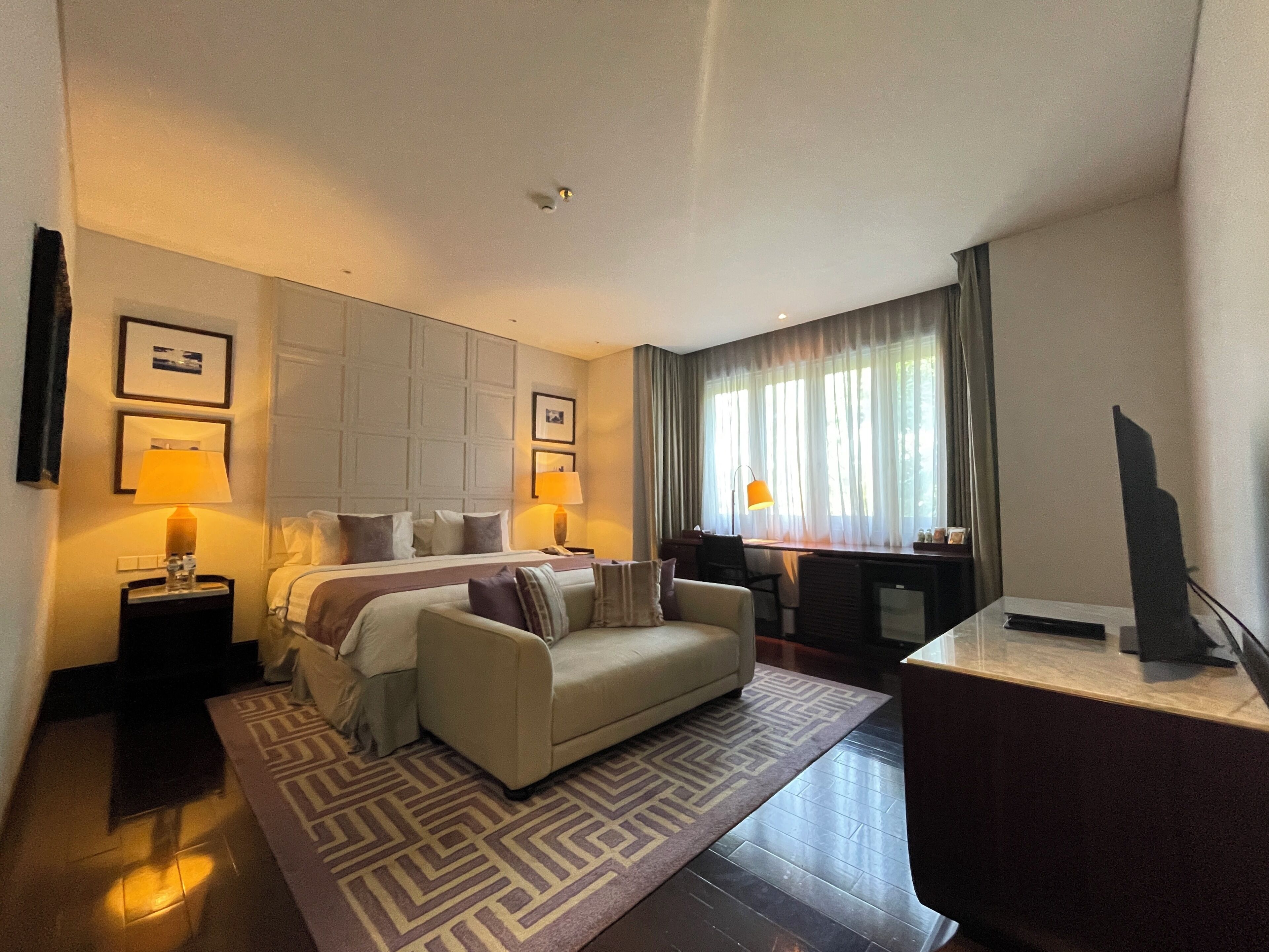 A hotel room with a bed, a sofa, a desk, and a TV.