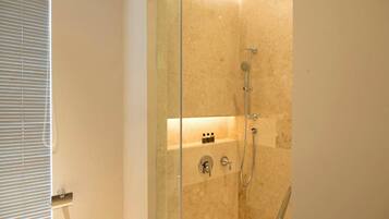 A glass-enclosed shower with a handheld showerhead and a wall-mounted faucet.