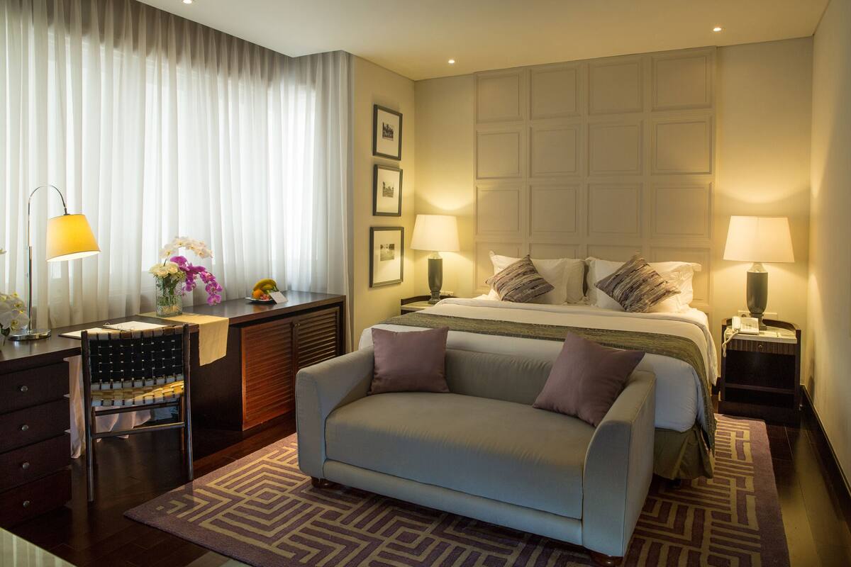 Une chambre d’hôtel comprenant un lit, deux tables de chevet avec des lampes, un canapé, un bureau avec une chaise et une commode.