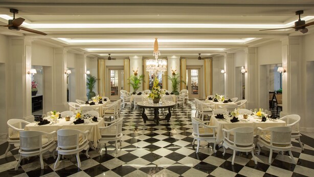 Une salle à manger élégante, avec des chaises et des tables blanches, un lustre et un sol à carreaux.