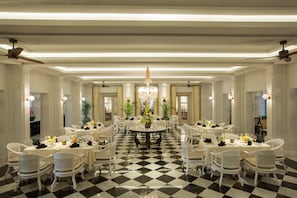 Un comedor elegante con sillas y mesas blancas, un candelabro y un suelo a cuadros.