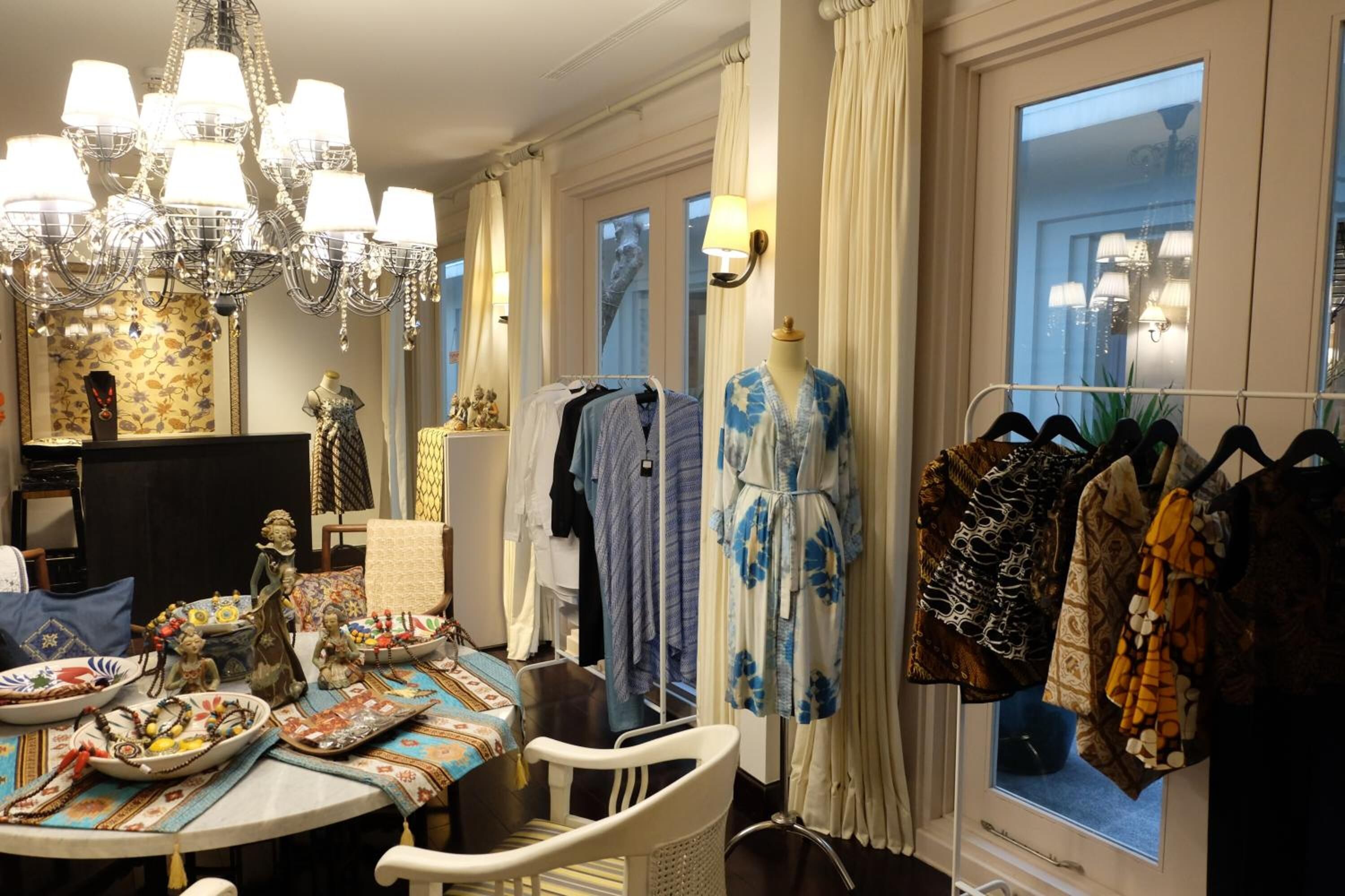 Quarto com lustre, mesa com objetos decorativos, janela com cortinas e um cabideiro com roupas.