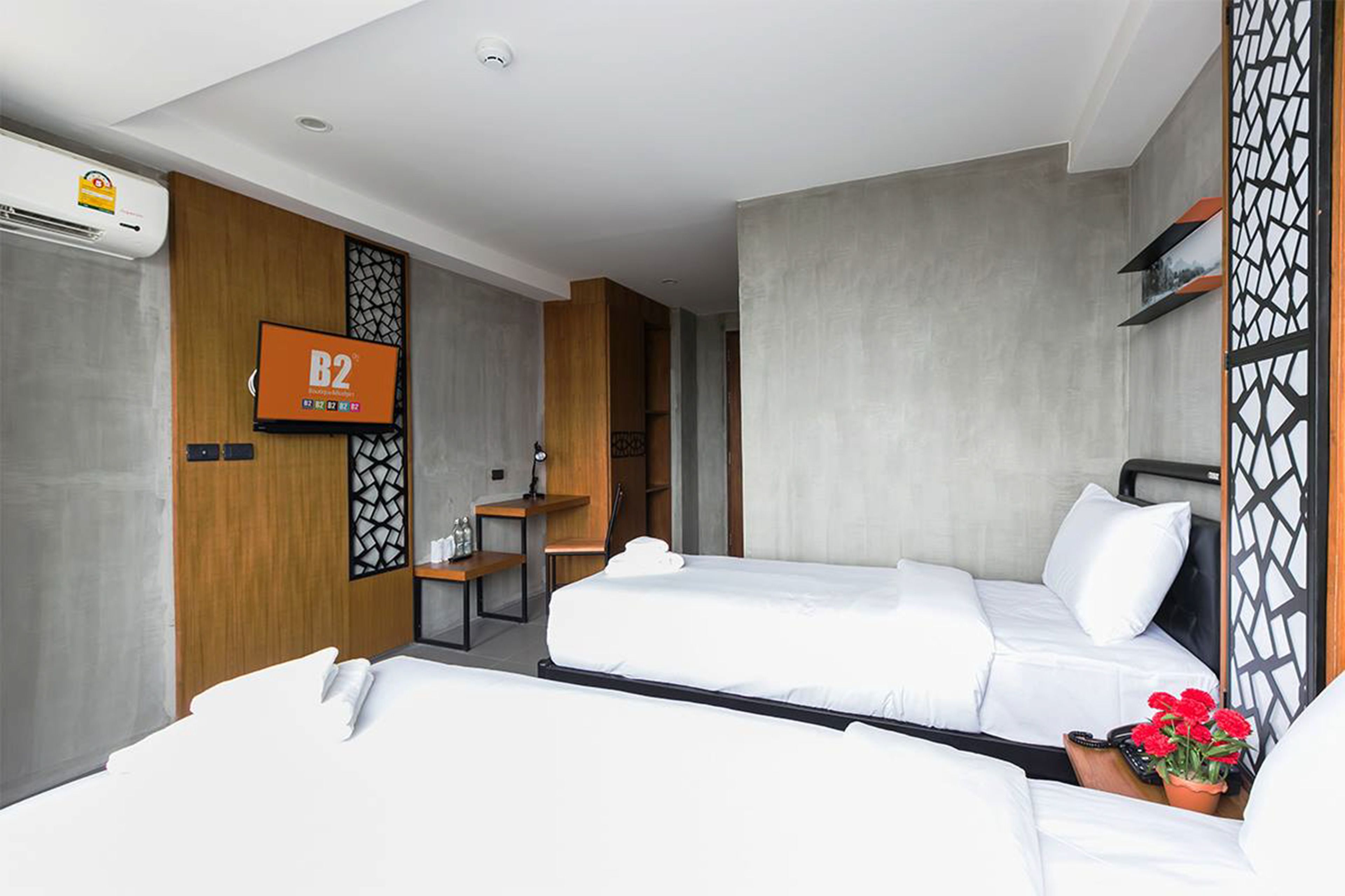 Habitació d'hotel amb dos llits, una taula de treball, una televisió i una pantalla decorativa.