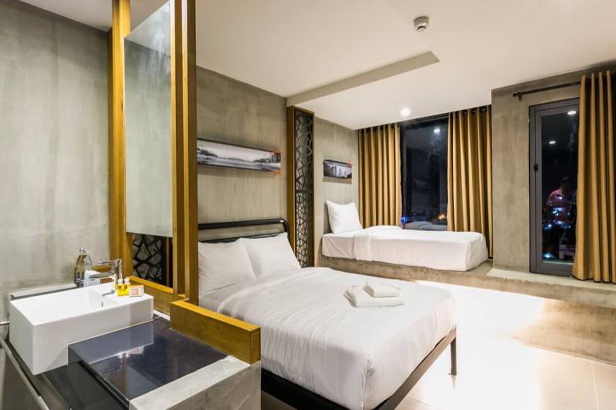 Ein modernes Hotelzimmer mit einem großen Bett, einem separaten Schlafbereich, einem Badezimmer mit Waschbecken und Blick auf die beleuchtete Stadt bei Nacht.