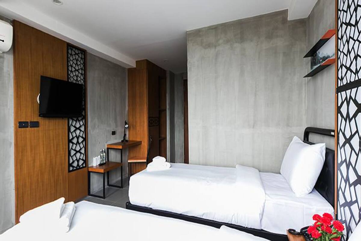 Ein Hotelzimmer mit zwei Betten, einem Fernseher, einem Holzschrank und einem dekorativen Raumteiler.