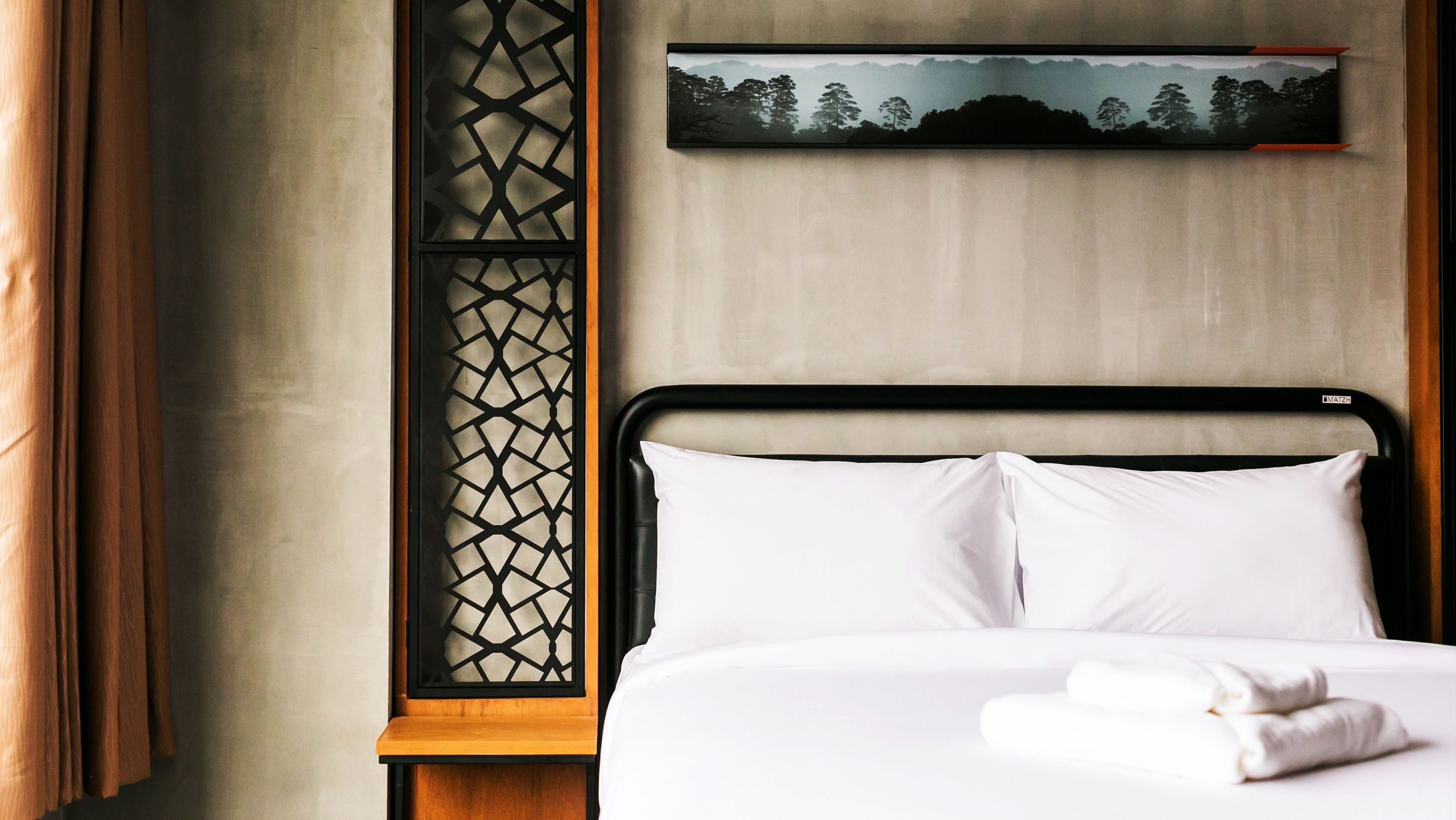 A neatly made bed with white linens and pillows, a wooden headboard, and a wall-mounted picture of a forest scene.
