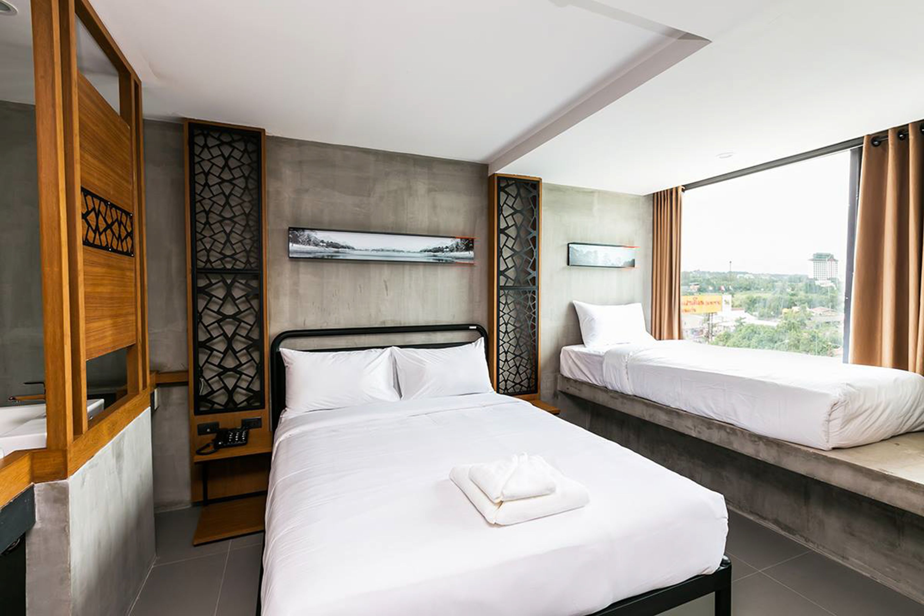 Habitación de hotel con una cama grande, una cama más pequeña, una ventana con vistas a la ciudad y un panel decorativo en la pared.
