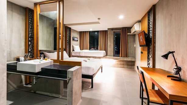 A modern hotel room with a large bed, a separate sitting area with a desk and chair, a large mirror, and a bathroom with a sink and vanity. - B2 Khon Kaen Boutique & Budget Hotel (Khon Kaen)