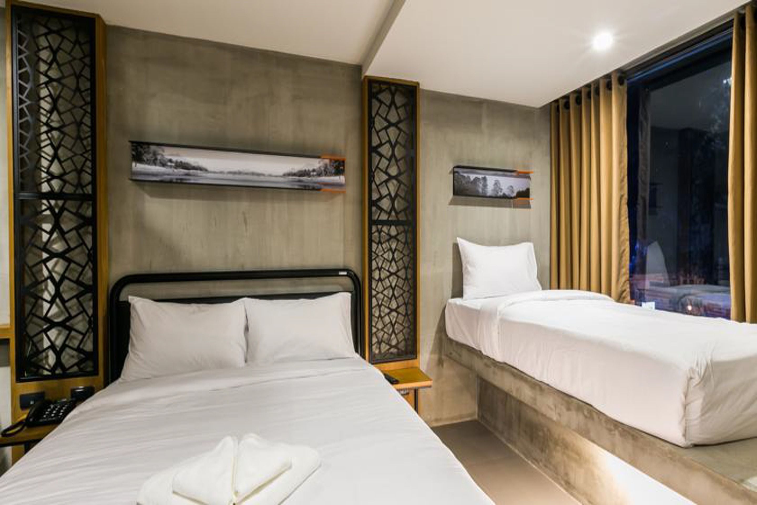 A hotel room with two beds, a large window with curtains, and decorative wall panels.