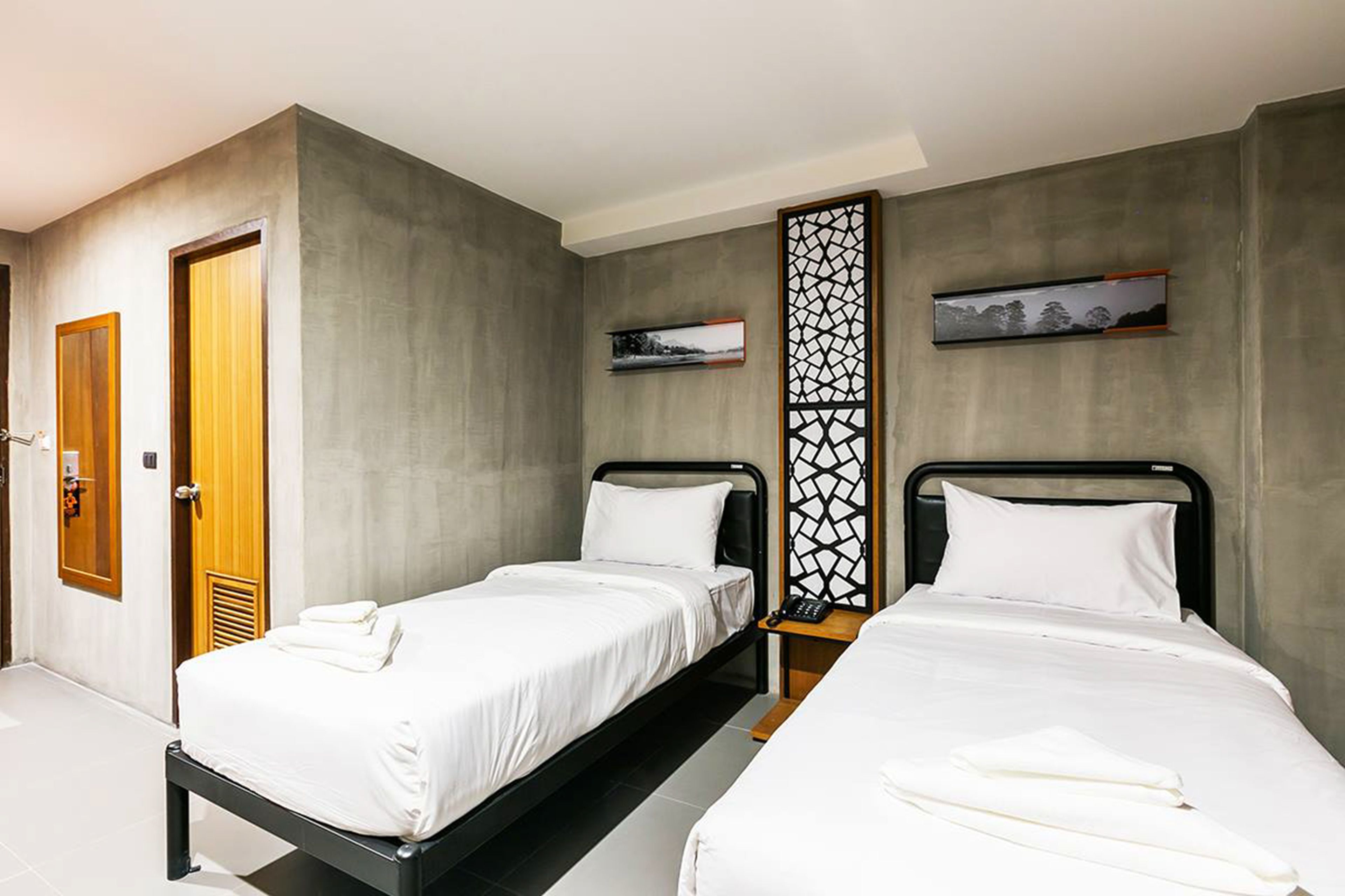 A hotel room with two single beds, a wooden door, a wall-mounted phone, and a decorative panel.