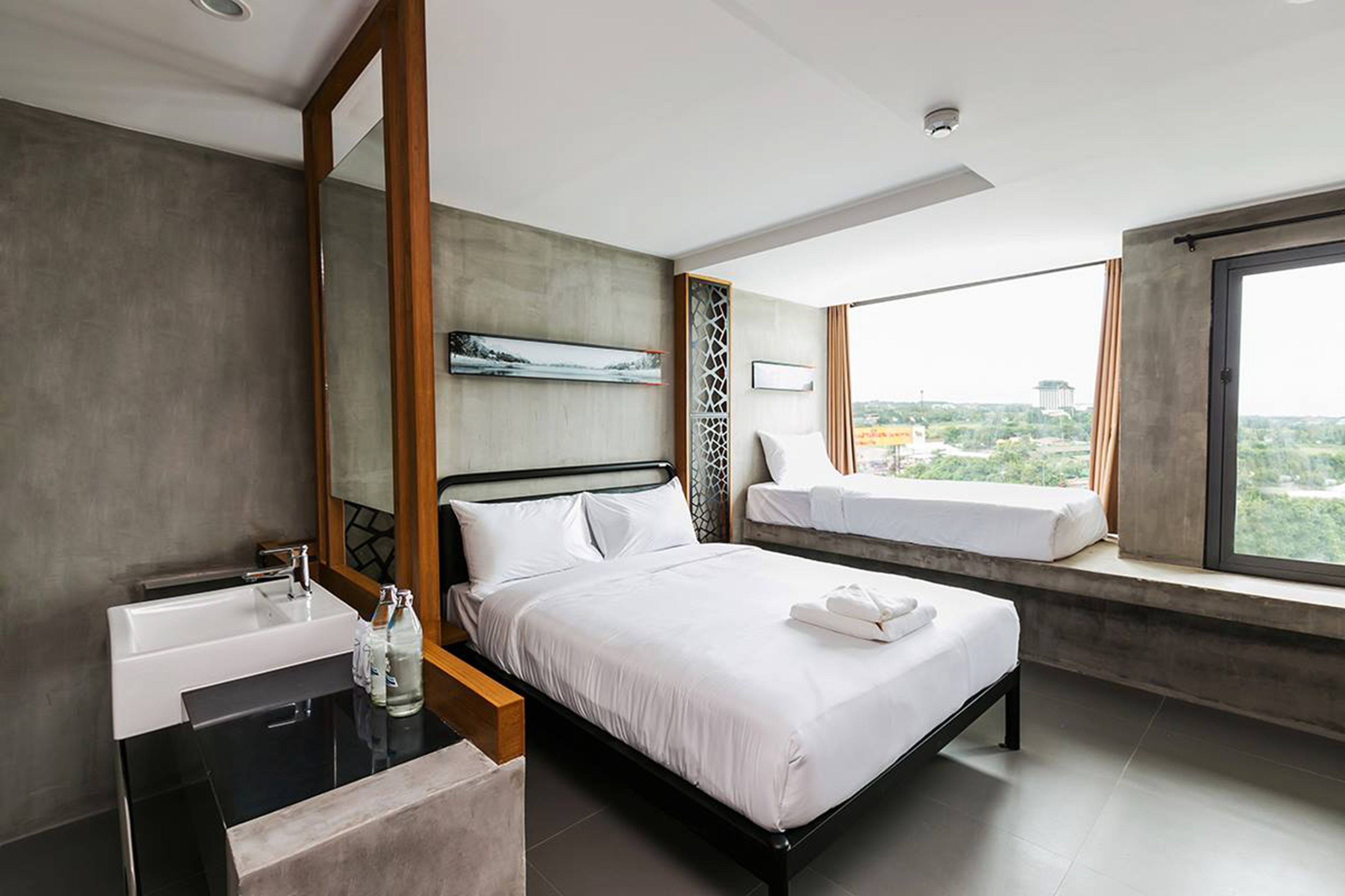 Una habitación de hotel moderna con una cama grande, una mesita de noche con espejo, un ventanal con vistas y un baño con lavabo y espejo.