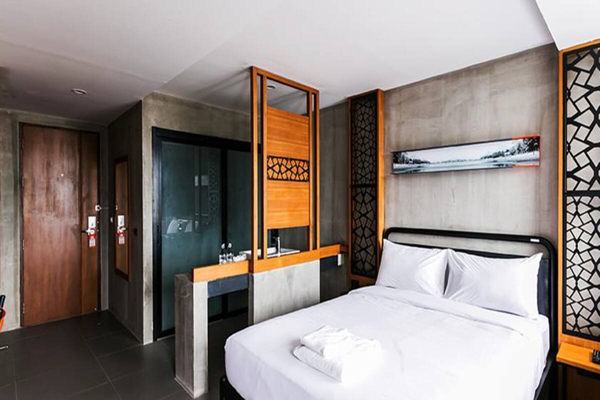Ein modernes Hotelzimmer mit einem großen Bett, einem Holztisch, einer Duschkabine und Blick auf eine verschneite Landschaft.