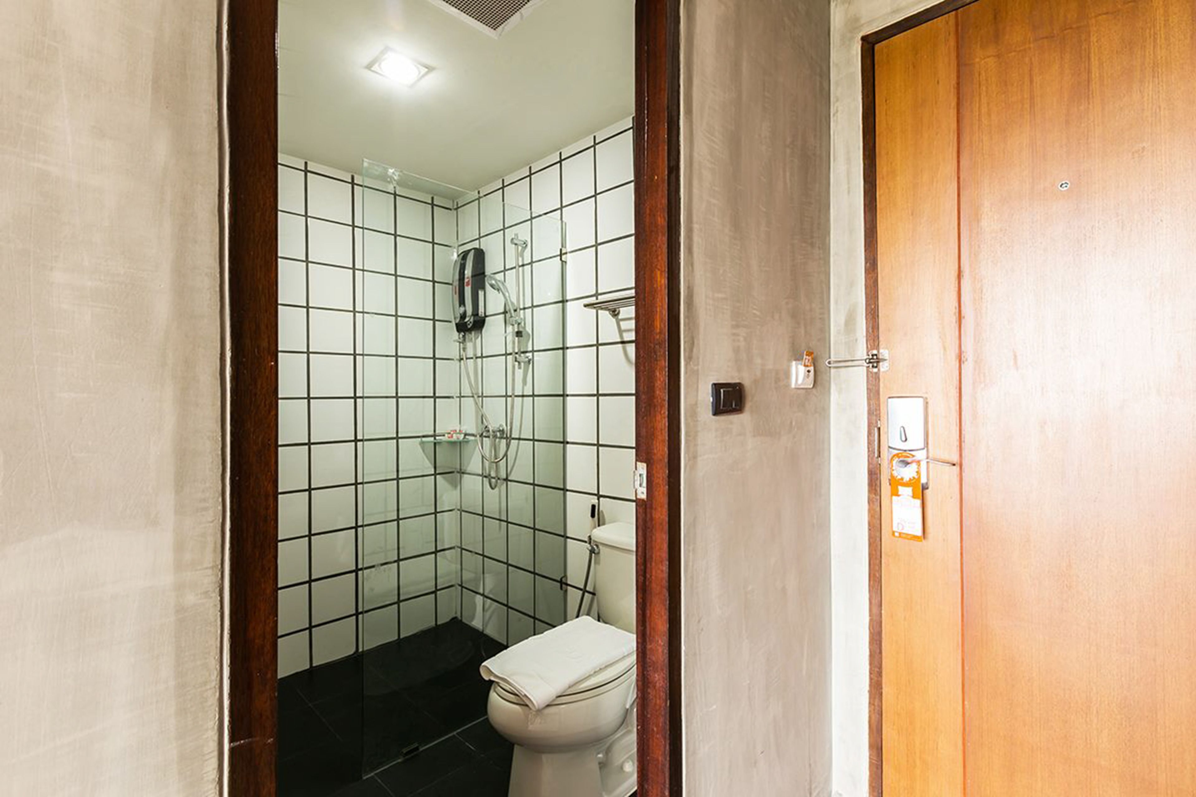 A small, tiled bathroom with a shower, toilet, and a wooden door.