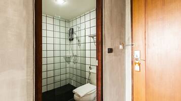A small, tiled bathroom with a shower, toilet, and a wooden door.