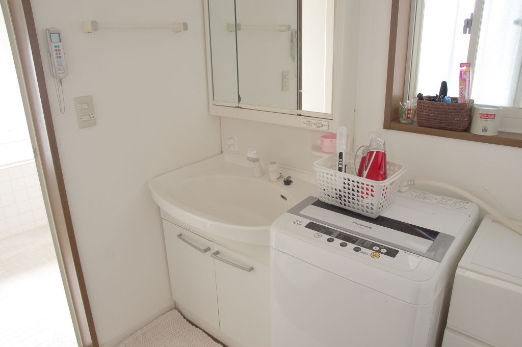 A small bathroom with a white sink, a mirror, a washing machine, and a basket with toiletries.