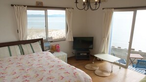 A bedroom with a bed, a TV, a small table, and a view of the beach. - Guest House Lohas Home (Akashi)