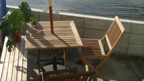 A wooden table and chair set under a beach umbrella on a balcony with a view of the ocean. - Guest House Lohas Home (Akashi)