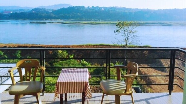 A terrace with two chairs and a table overlooking a body of water and distant hills.