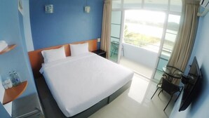 A hotel room with a large bed, a small desk, a chair, and a balcony with a view.