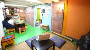 A small room with a green carpet, a laptop on a table, and a person sitting on a stool. - Yadoya Guest House Orange - Hostel (Tokyo)