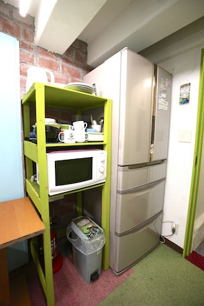 Cozinha compacta com micro-ondas, frigorífico e uma estante com louças e máquina de café.