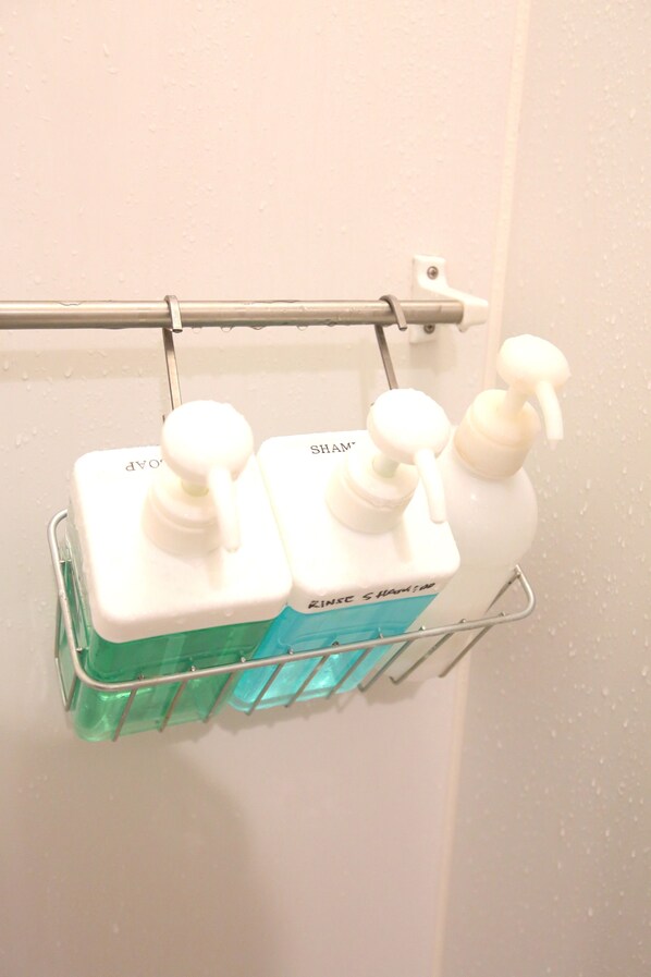 Une salle de bain avec un porte-serviettes en métal sur lequel sont posés trois flacons de shampoing et d’après-shampoing.