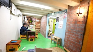 A room with a green floor, a Dell laptop on a table, and a person sitting on a stool. - Yadoya Guest House Orange - Hostel (Tokyo)