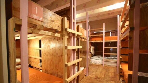 A bunk bed room with wooden bunk beds, a wooden floor, and a number sign on the wall. - Yadoya Guest House Orange - Hostel (Tokyo)