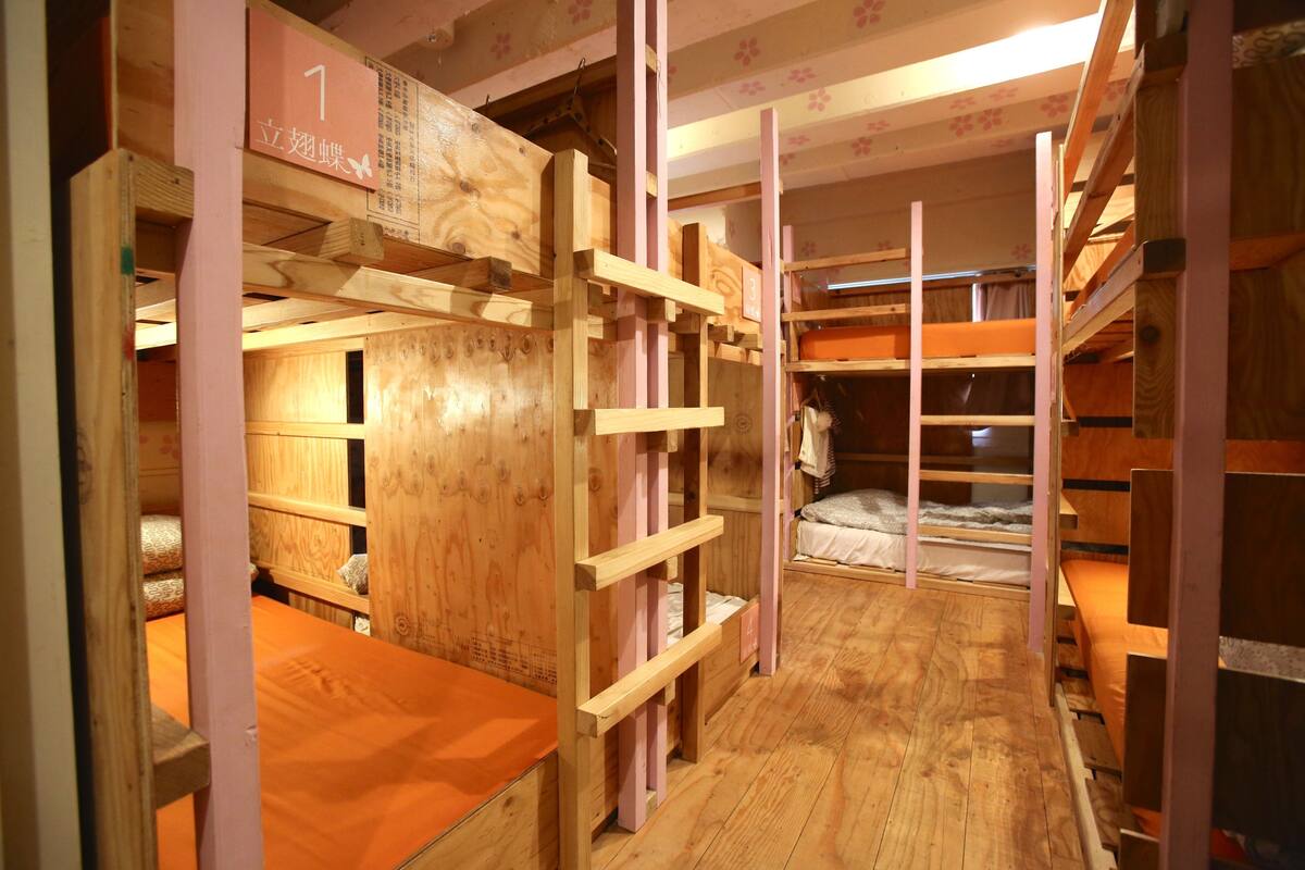 Une chambre avec des lits superposés en bois, un plancher en bois et un panneau indiquant le numéro de la chambre sur le mur.