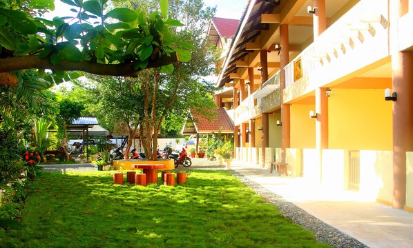 A courtyard with a grassy area, trees, and a building with a tiled roof.