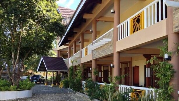 Un hotel con un espacio exterior techado, varios balcones y un camino de grava que lleva a la entrada.