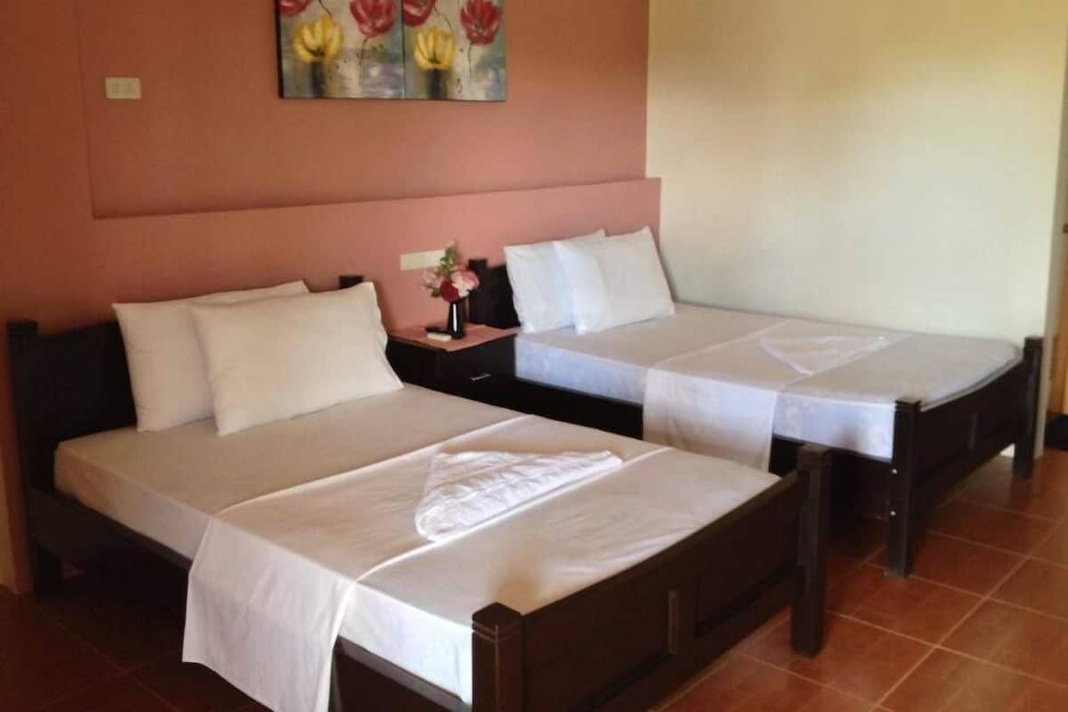A hotel room with two beds, each with white linens and a small table with a vase of flowers.