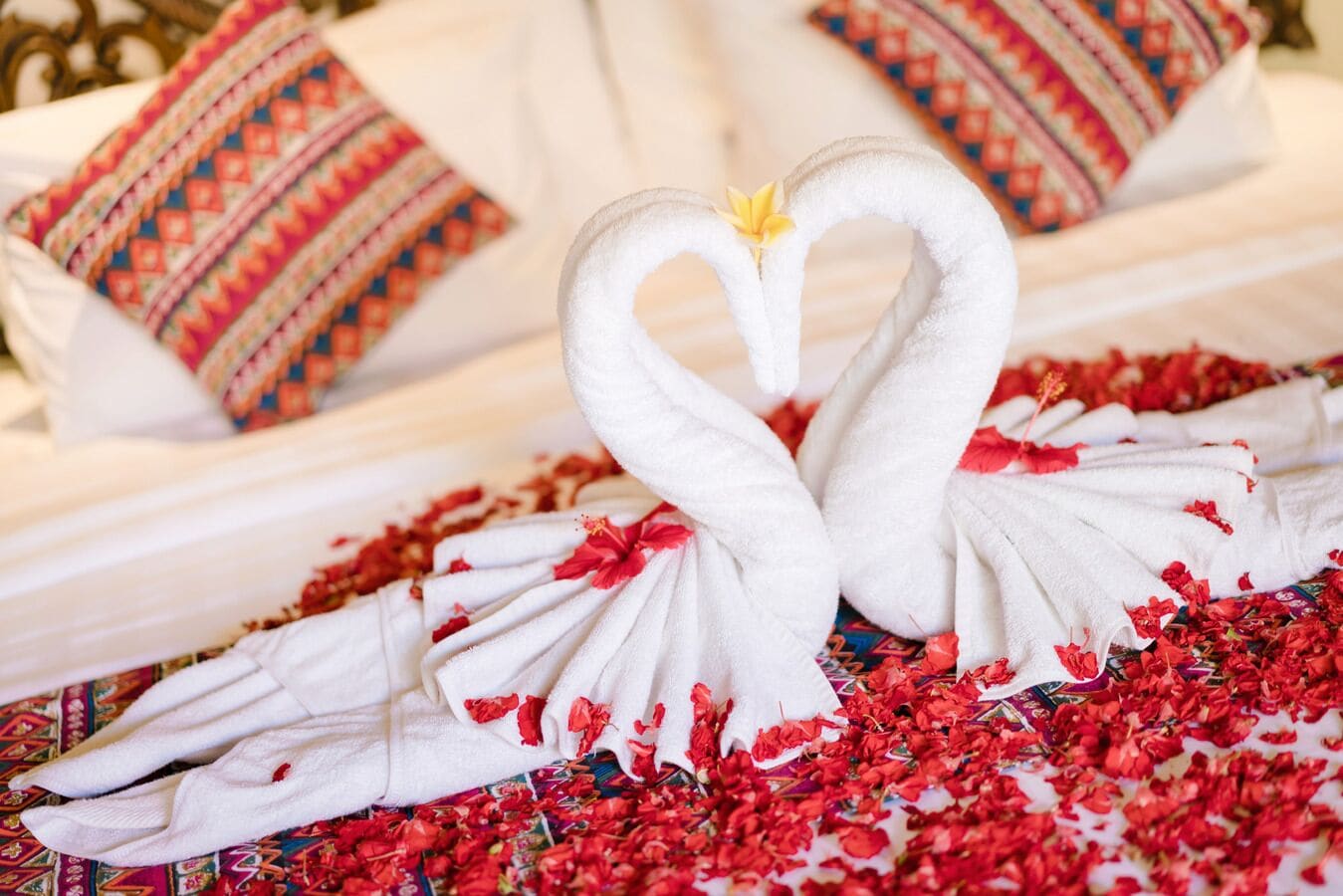 Un lit avec du linge de lit blanc et un cygne décoratif fait de serviettes.