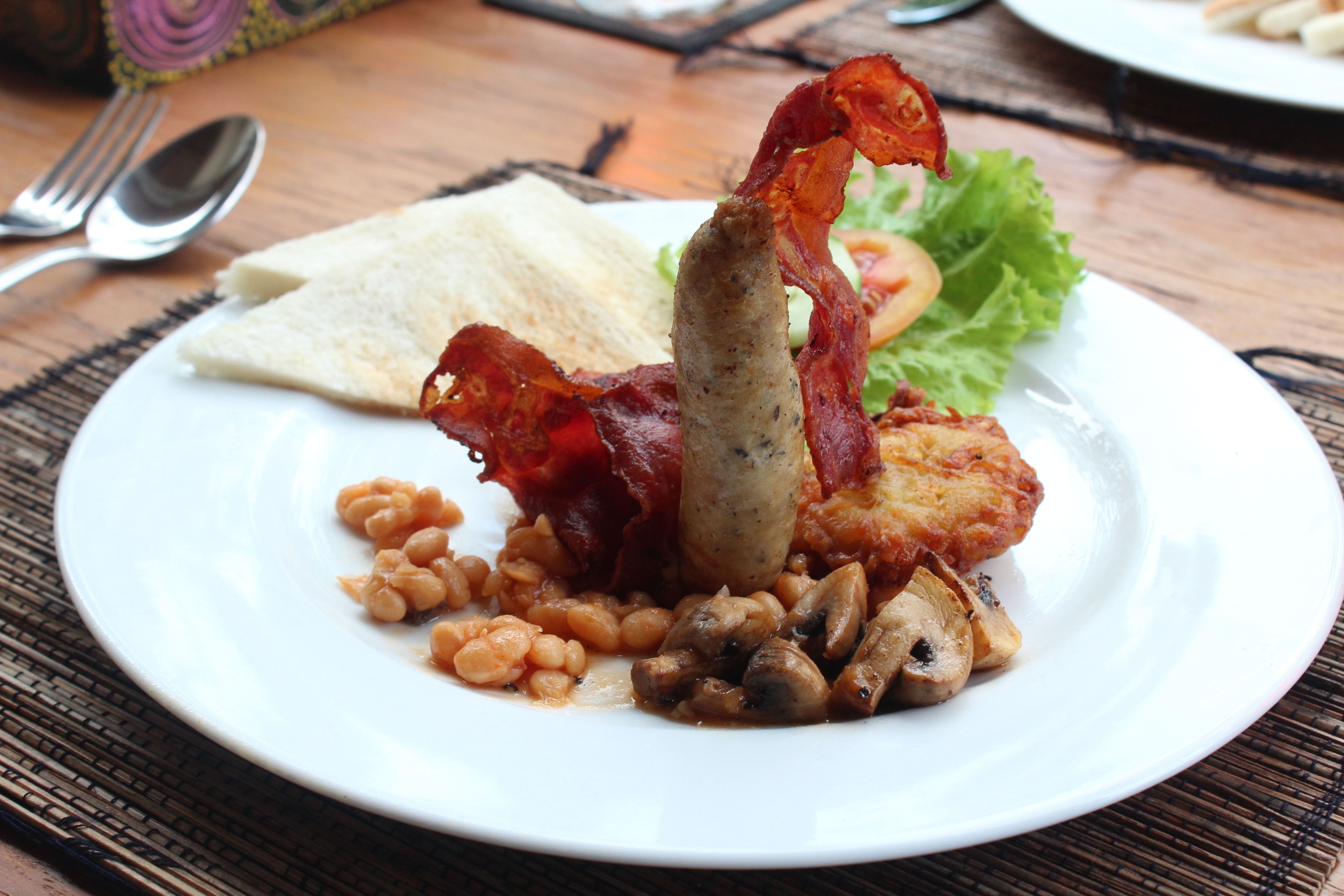 A plate of food with beans, bacon, mushrooms, and a sausage on a white plate.