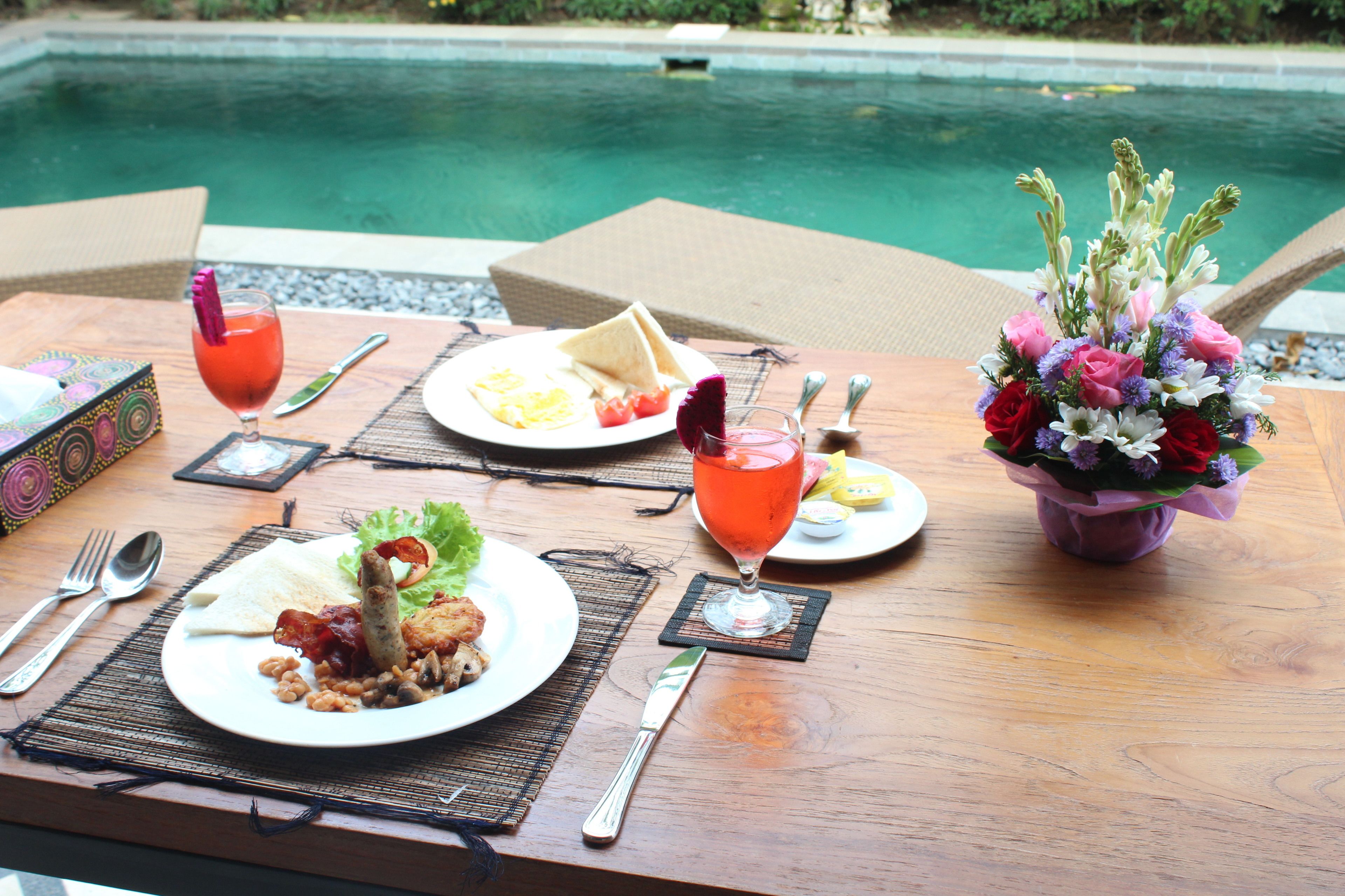 A dining table with plates of food, cutlery, and a drink, set against a poolside backdrop.