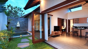 Une maison moderne avec une porte vitrée donnant sur un espace de vie, un petit jardin extérieur et une cuisine dotée de meubles en bois.