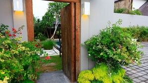 Une porte d’entrée en bois qui mène à un jardin agrémenté de diverses plantes et doté d’un sentier.