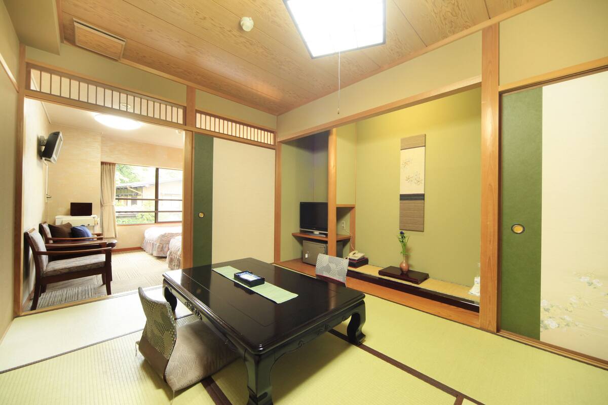A traditional Japanese room with tatami flooring, a low table, a sofa, and a television.