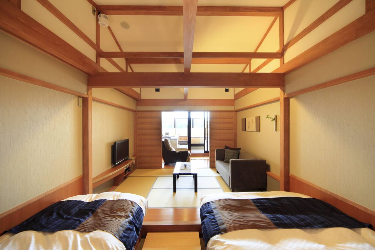 A traditional Japanese-style room with tatami flooring, two beds, a television, and a sliding door leading to a balcony.