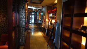 A corridor with patterned wallpaper, a wooden bench, a reception desk, and a wall-mounted display. - HOTEL Salle De Bain - Adults Only (Osaka)