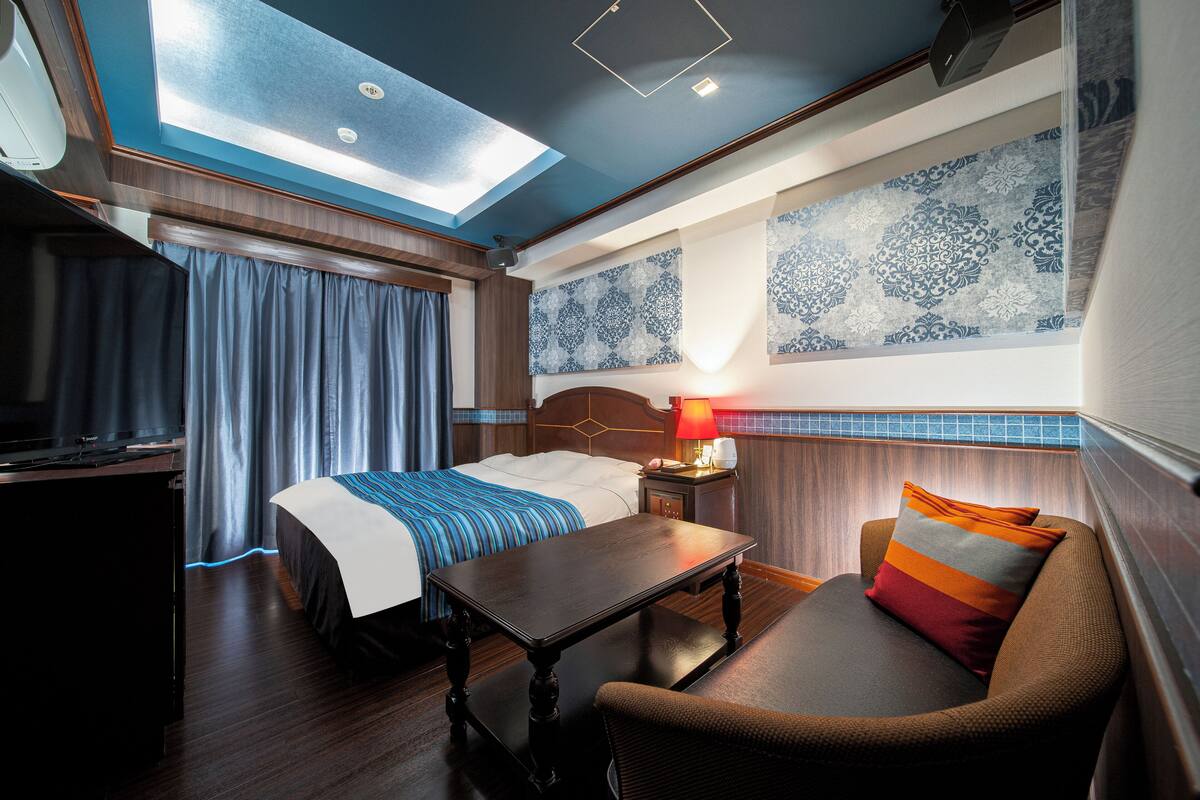 A hotel room with a bed, a table, a sofa, a TV, and a ceiling light.
