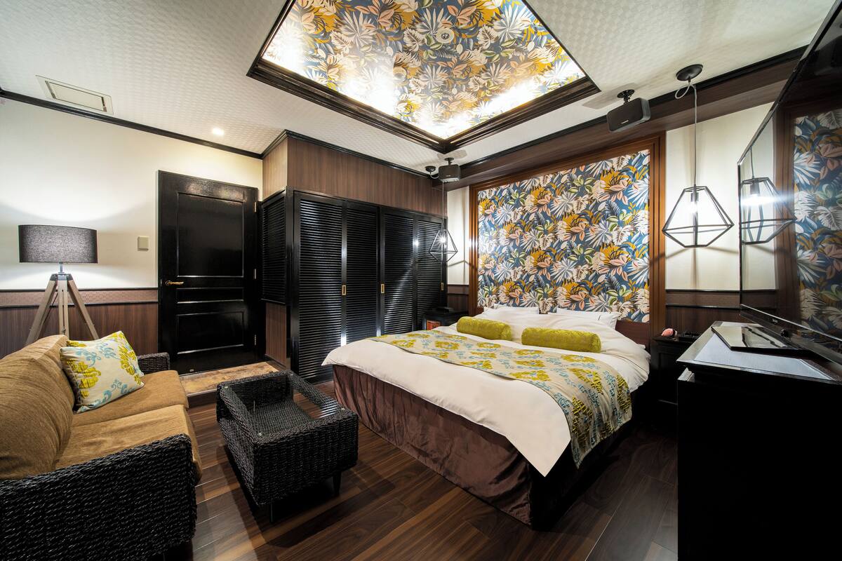 A modern hotel room with a large bed, a sofa, a desk, and a ceiling with a floral design.