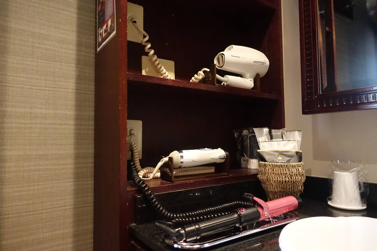 A bathroom vanity with a hairdryer, a curling iron, and a towel rack.