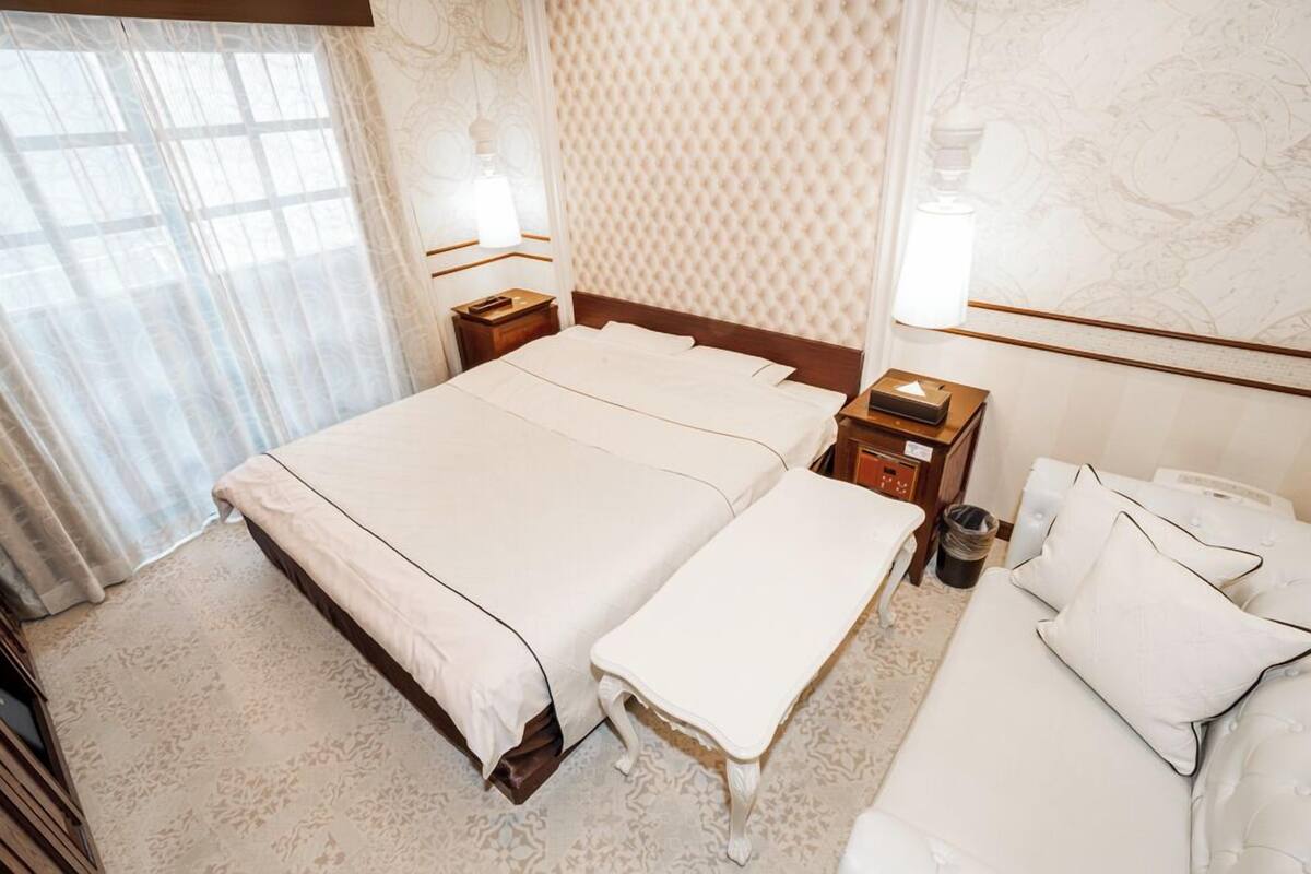 A hotel room with a large bed, a bench, a sofa, and a nightstand with a lamp.